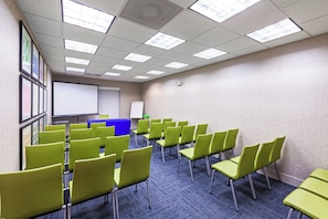 A conference room with rows of green chairs, a whiteboard, and a projector screen.
