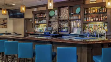 Un espace bar comprenant un comptoir, des tabourets de bar et des étagères remplies de bouteilles et de verres.