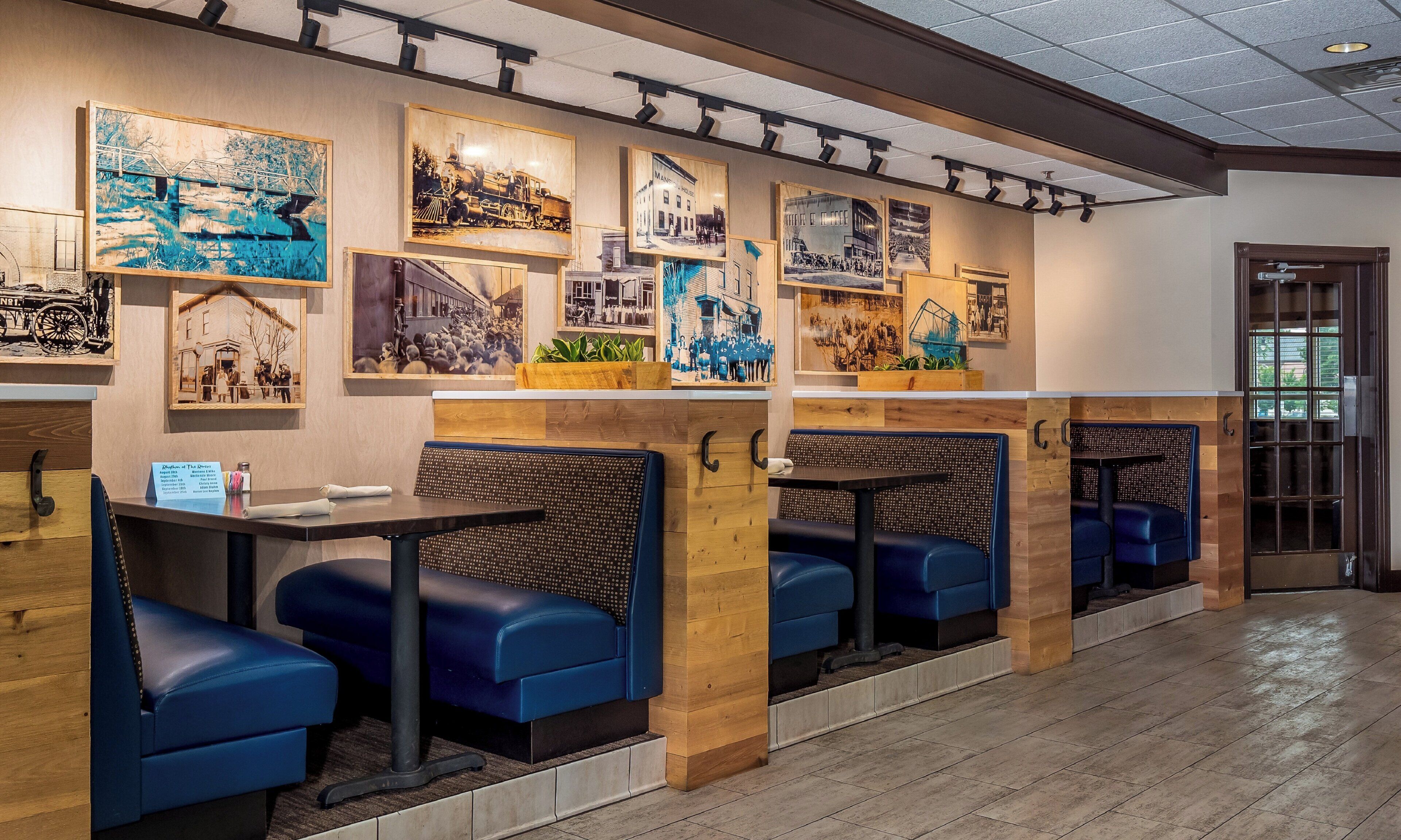 A restaurant interior with wooden booths, black cushioned seating, and wall-mounted artwork.