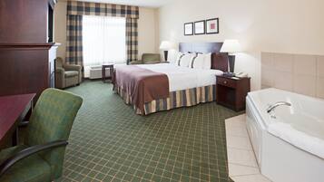 A hotel room with a bed, two bedside tables, a chair, a desk, a desk lamp, a telephone, a wall-mounted TV, and a bathroom with a bathtub and toilet.