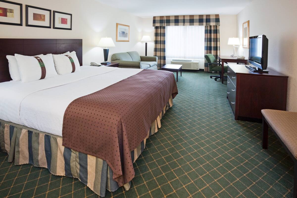 A hotel room with a large bed, a desk with a television, a chair, and a sofa.