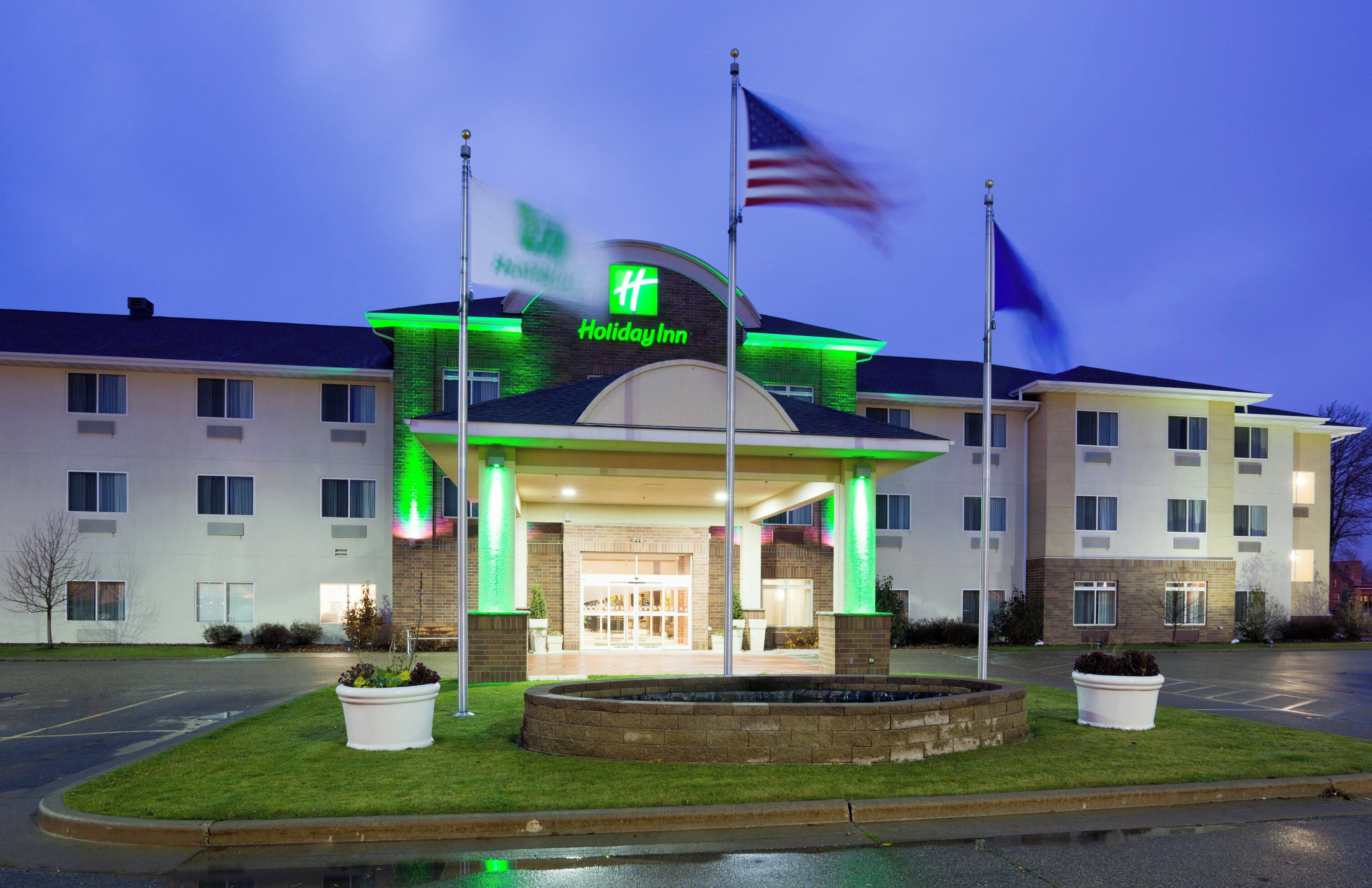 Een Holiday Inn hotel met een bakstenen gevel, een groen verlicht bord en een wimpelpaal met de Amerikaanse vlag.