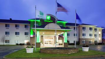 A Holiday Inn hotel with a brick facade, a green illuminated sign, and a flagpole with an American flag.