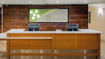 A reception desk with two computer monitors, a framed sign above, and a wooden wall.