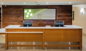 A reception desk with two computer monitors, a framed sign above, and a wooden wall. - Holiday Inn Conference Ctr Marshfield by IHG (Marshfield)