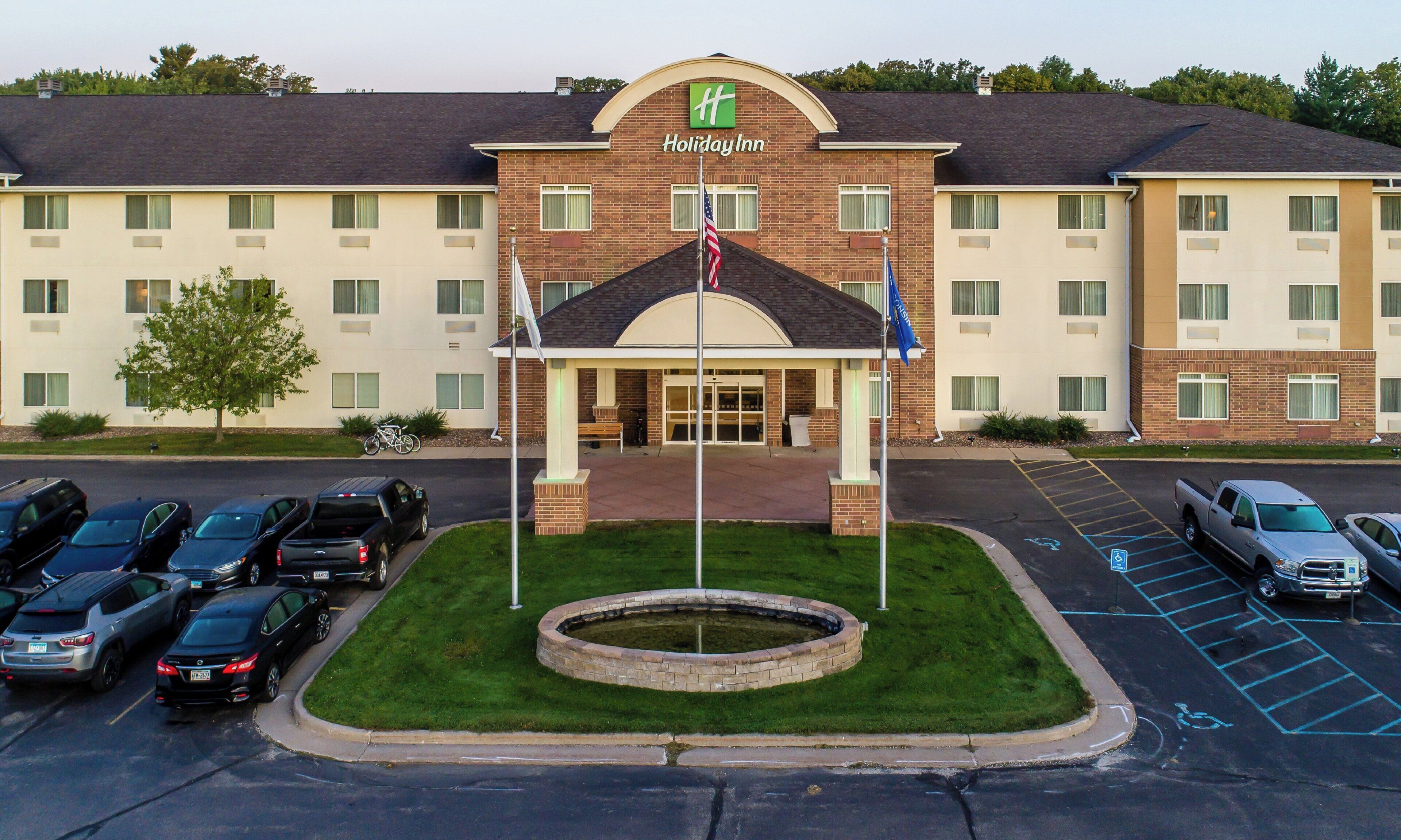 Un hôtel Holiday Inn avec une façade en briques, une entrée centrale et un parking où sont stationnés divers véhicules.