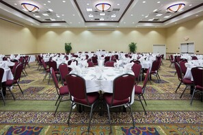 A banquet hall with round tables, red chairs, and white tablecloths.
