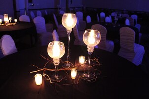 Una mesa con velas encendidas y copas de vino, rodeada de sillas.