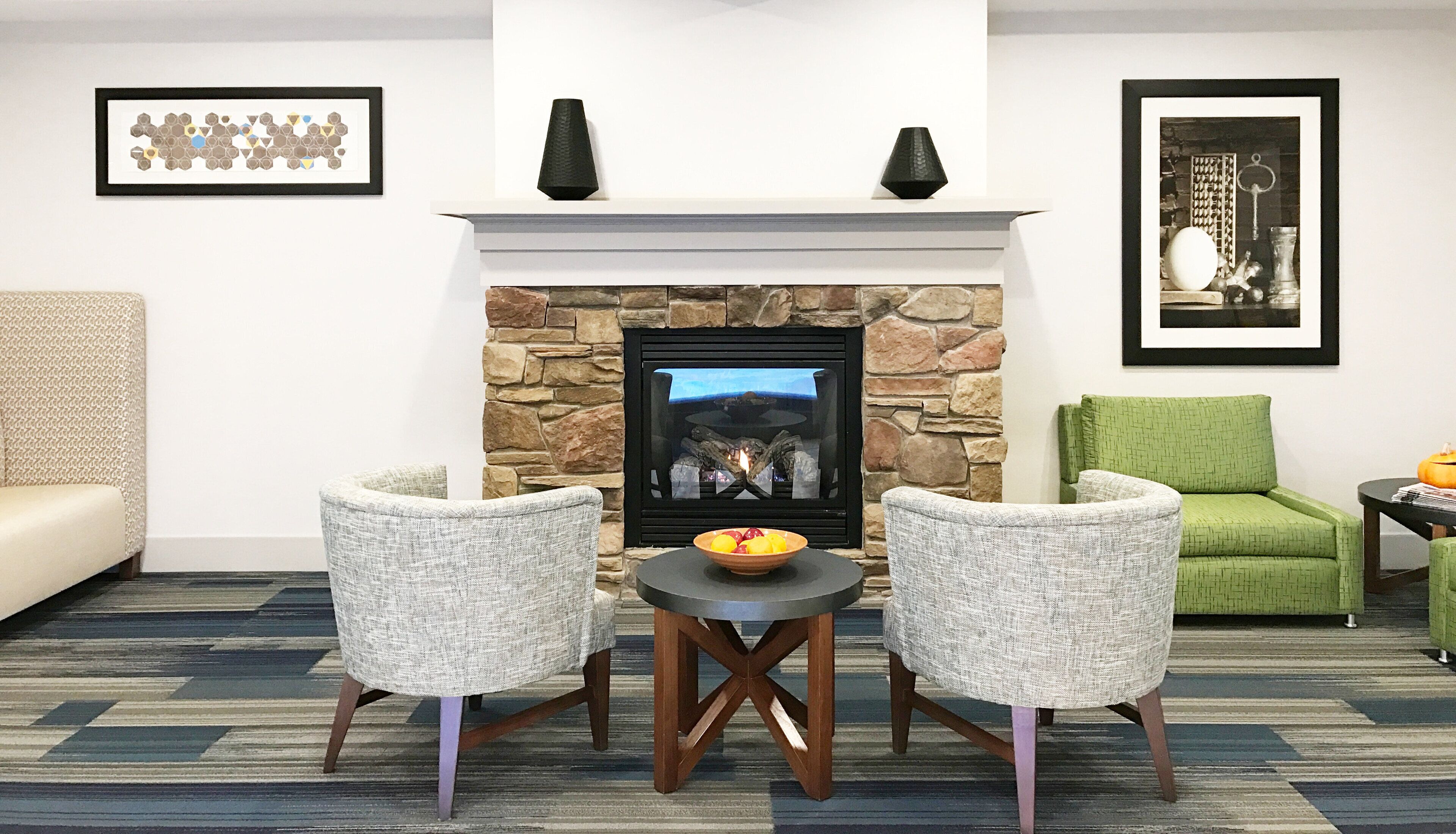 A living room with a stone fireplace, two upholstered chairs, a small round table, and a green armchair.