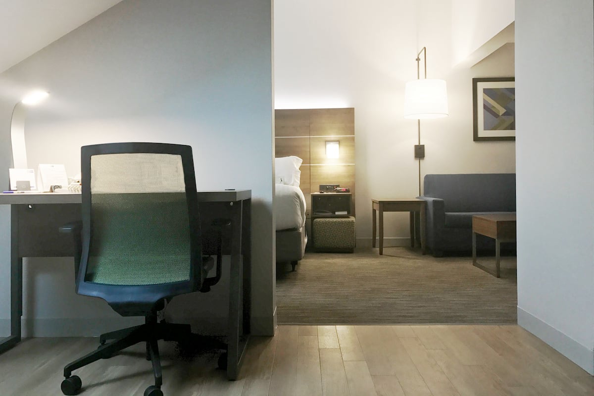 Une chambre d’hôtel équipée d’un bureau, d’une chaise de bureau, d’un lit, d’une table de chevet, d’une lampe et d’un tableau encadré au mur.