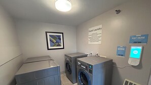 Un espace buanderie équipé de deux machines à laver, d’un sèche-linge, d’un terminal de paiement et d’un panneau indiquant que cet espace est réservé à la buanderie des clients.