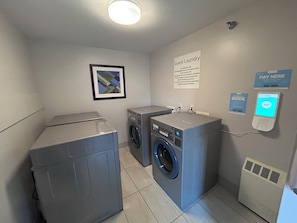 Un espace buanderie équipé de deux machines à laver, d’un sèche-linge, d’un terminal de paiement et d’un panneau indiquant que cet espace est réservé à la buanderie des clients.