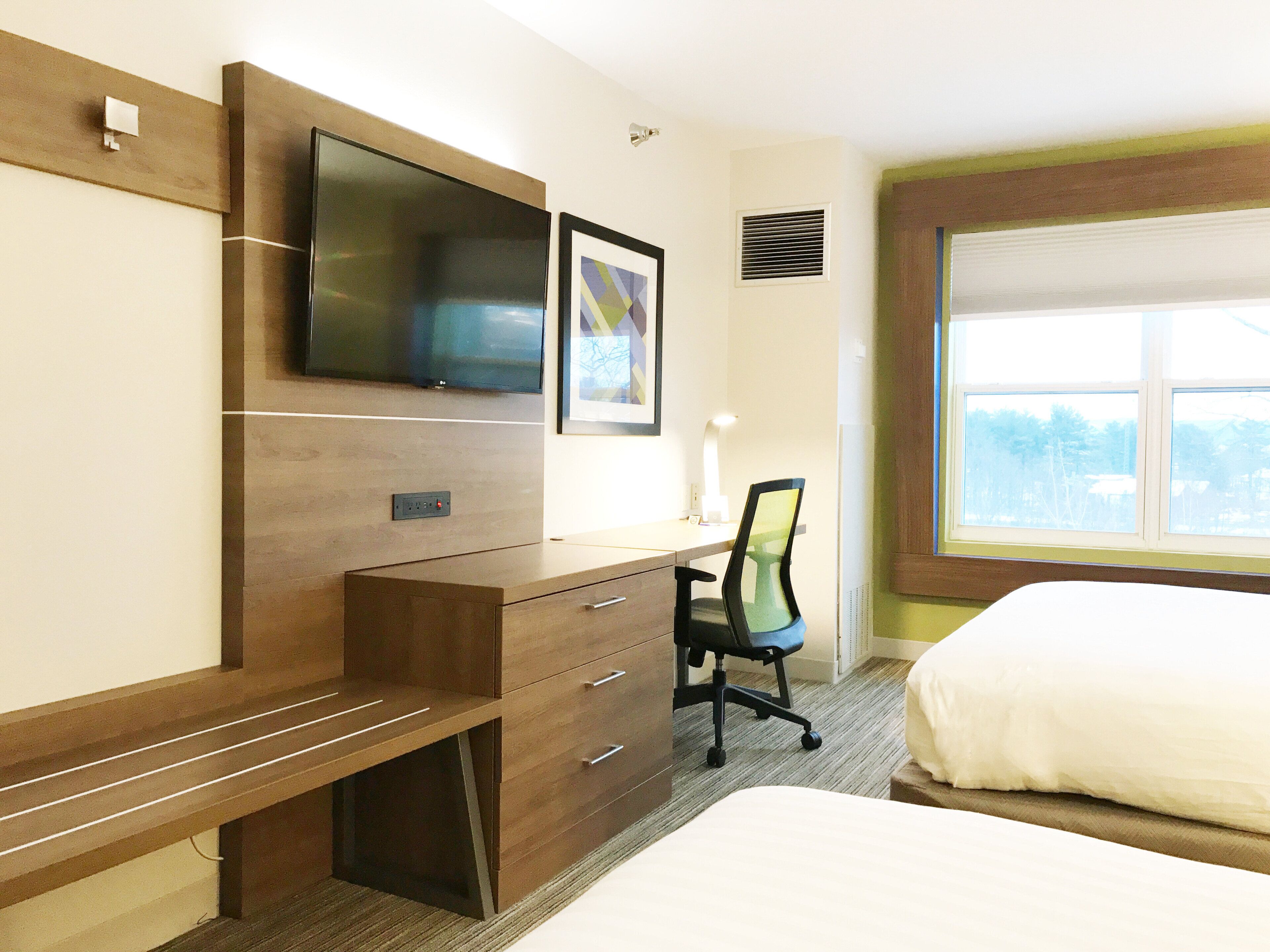 A hotel room with a bed, a desk with a chair, a television, and a window.