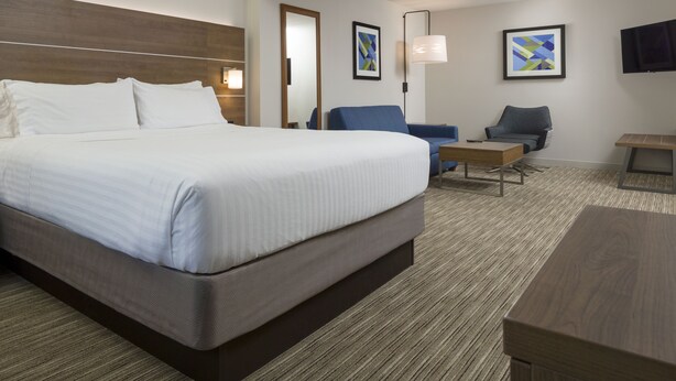 A hotel room with a large bed, two armchairs, a small table, and a TV on the wall. - Holiday Inn Express Hotel & Suites White River Junction by IHG (White River Junction)