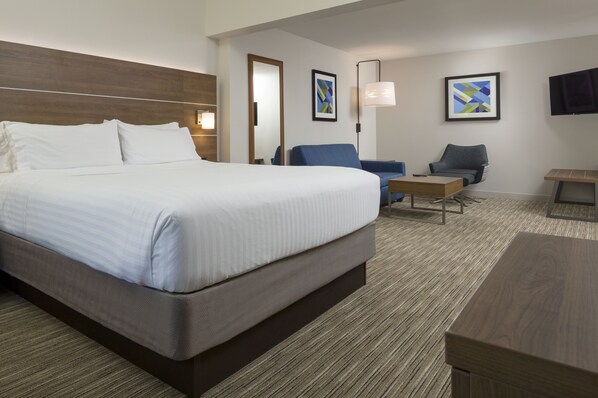Ein Hotelzimmer mit einem großen Bett, zwei Sesseln, einem kleinen Tisch und einem an der Wand befestigten Fernseher.