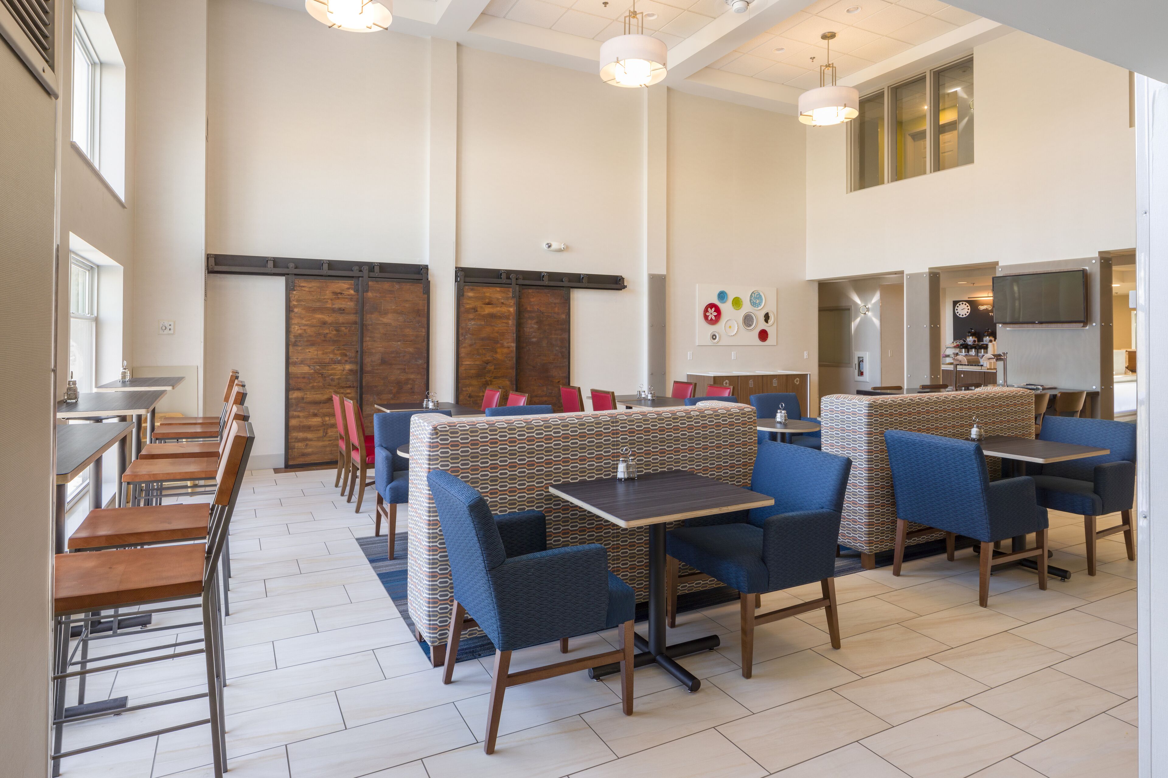 Un vaste espace dédié à la salle à manger, avec de hauts plafonds, des tables en bois et des banquettes rembourrées de tissu bleu.
