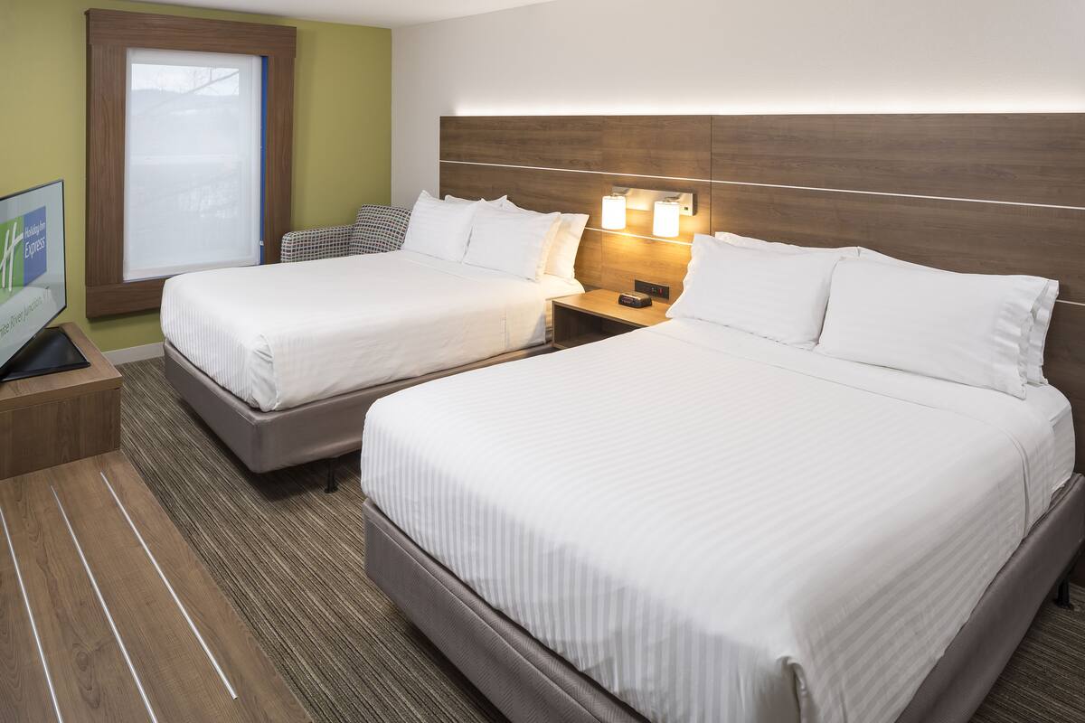 Une chambre d’hôtel avec deux lits, une tête de lit en bois, une table de chevet avec une lampe et un téléviseur posé sur un meuble.