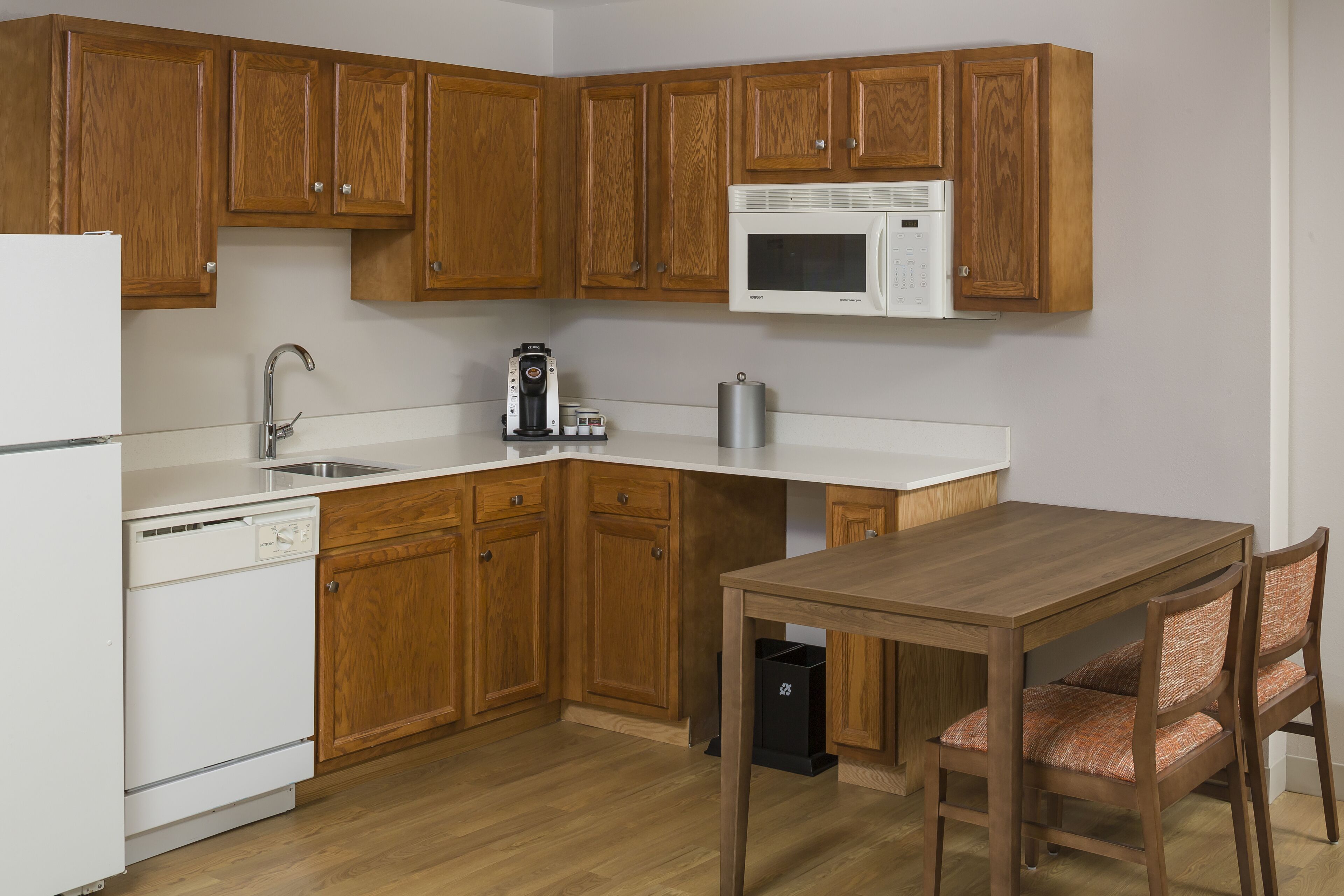 A kitchen with wooden cabinets, a microwave, a sink, a dishwasher, and a dining table with chairs.
