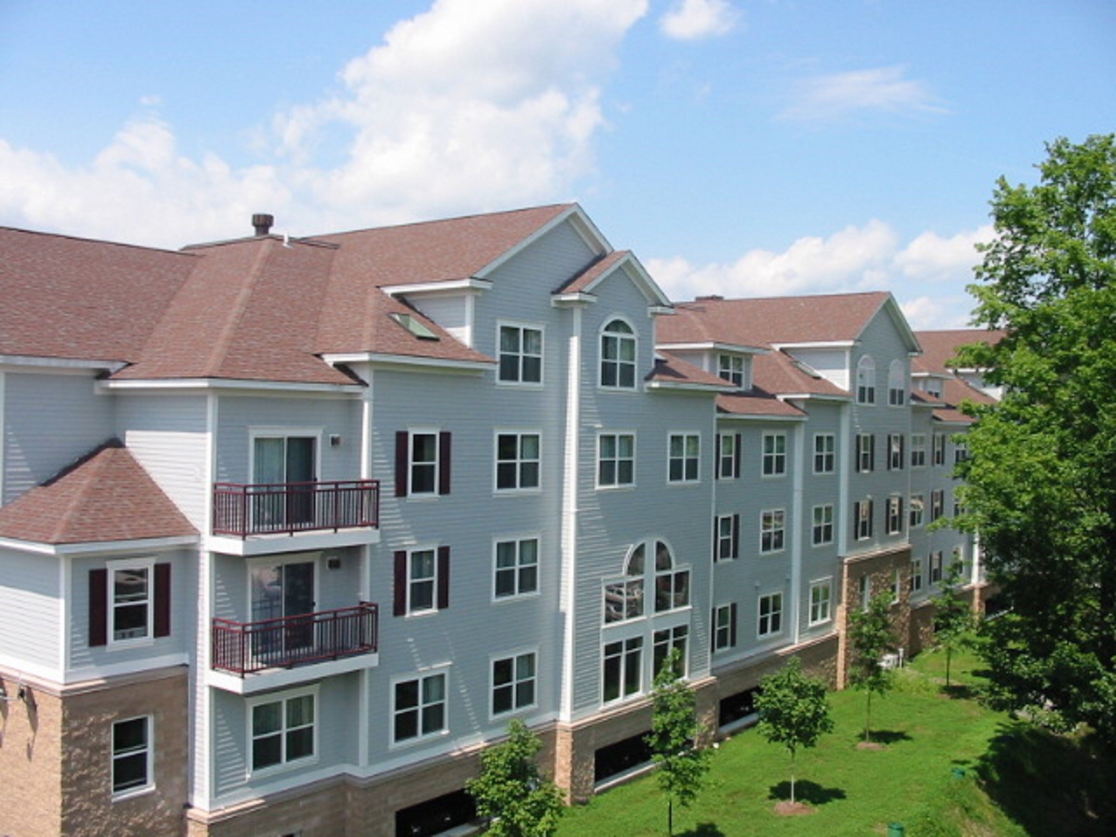 A multi-story residential building with a brick facade, multiple balconies, and a well-maintained lawn.