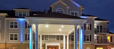 Un hotel de varios pisos con entrada cubierta, columnas y fachada bien iluminada.