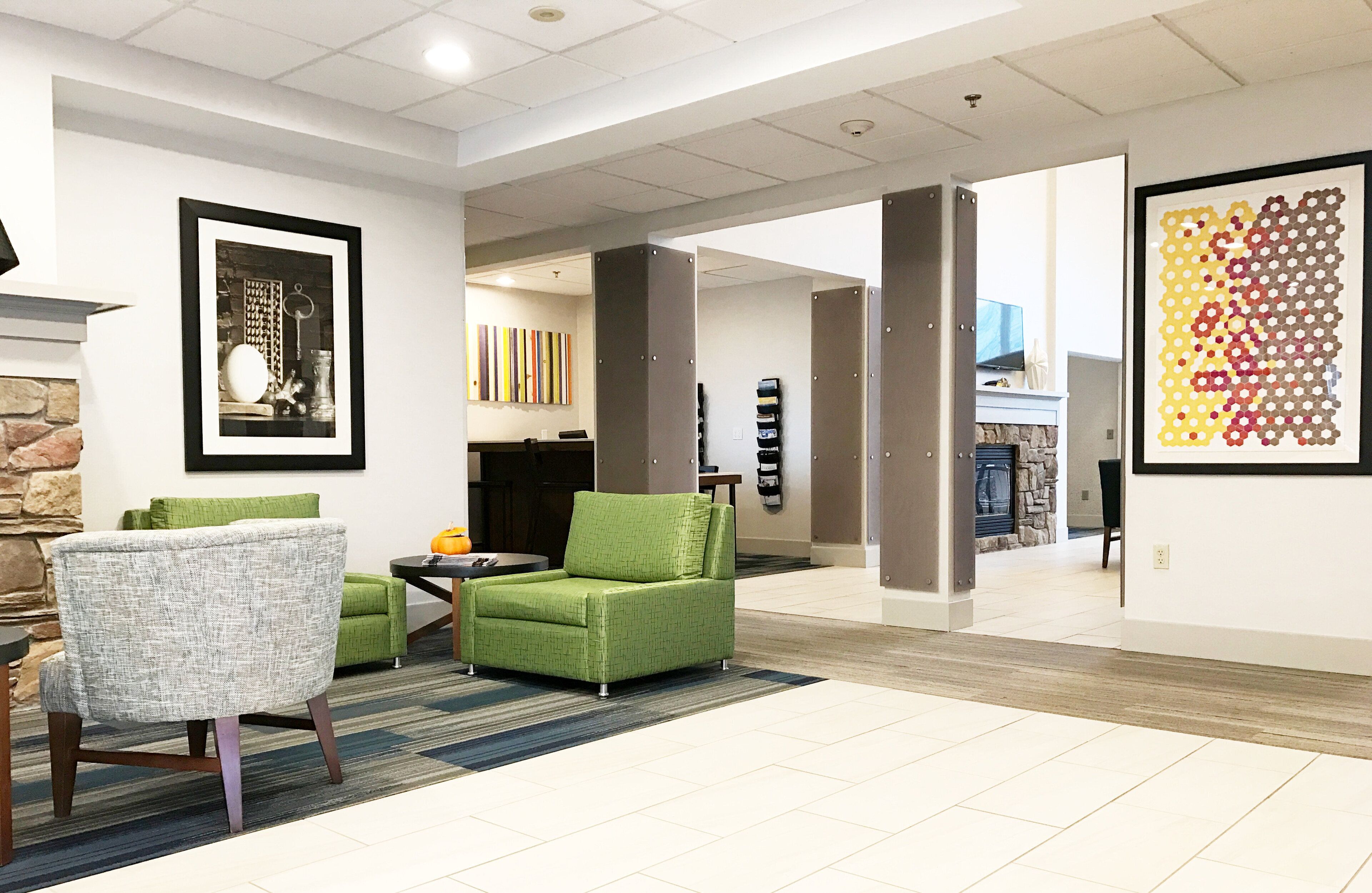 A modern interior with a fireplace, green armchairs, a framed picture, and a colorful abstract art piece.