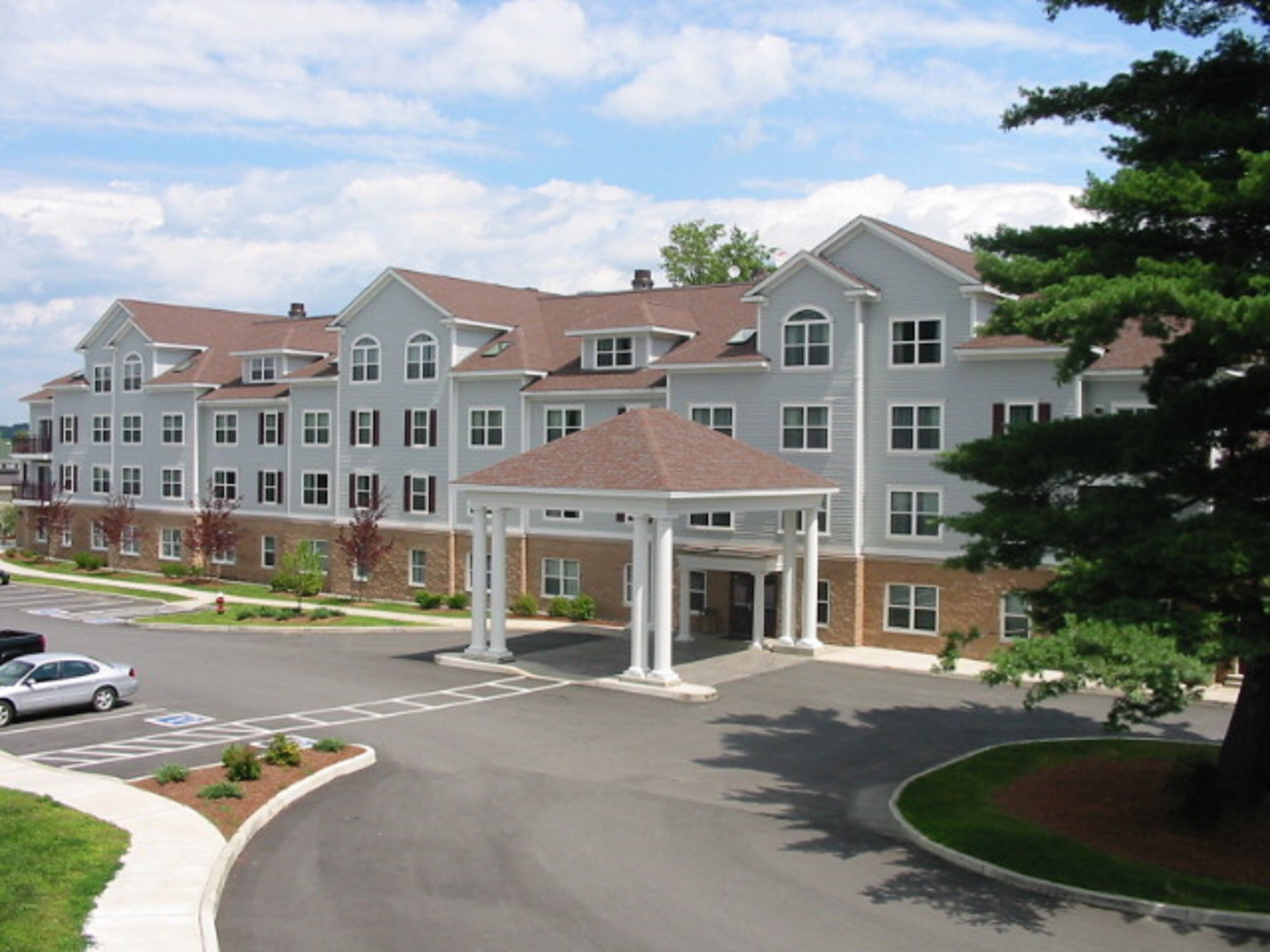 A multi-story hotel with a central entrance pavilion, parking lot, and landscaped areas.