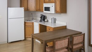 A compact kitchen with wooden cabinets, a white refrigerator, a microwave, a coffee maker, and a sink. - Holiday Inn Express Hotel & Suites White River Junction by IHG (White River Junction)