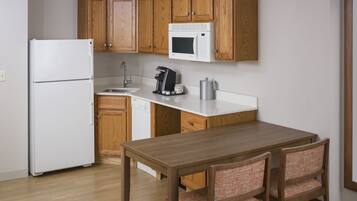 Una cocina compacta con armarios de madera, un refrigerador blanco, un microondas, una cafetera y un lavamanos.
