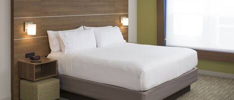 A neatly made bed with white linens, a wooden headboard, two bedside tables with lamps, and a small ottoman.