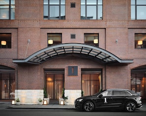 A hotel entrance with a brick facade, a curved overhang, and a black car parked in front.