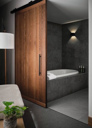 A modern bathroom with a wooden wardrobe, a bathtub, a wall-mounted light, and a potted plant. - 1 Hotel San Francisco (San Francisco)