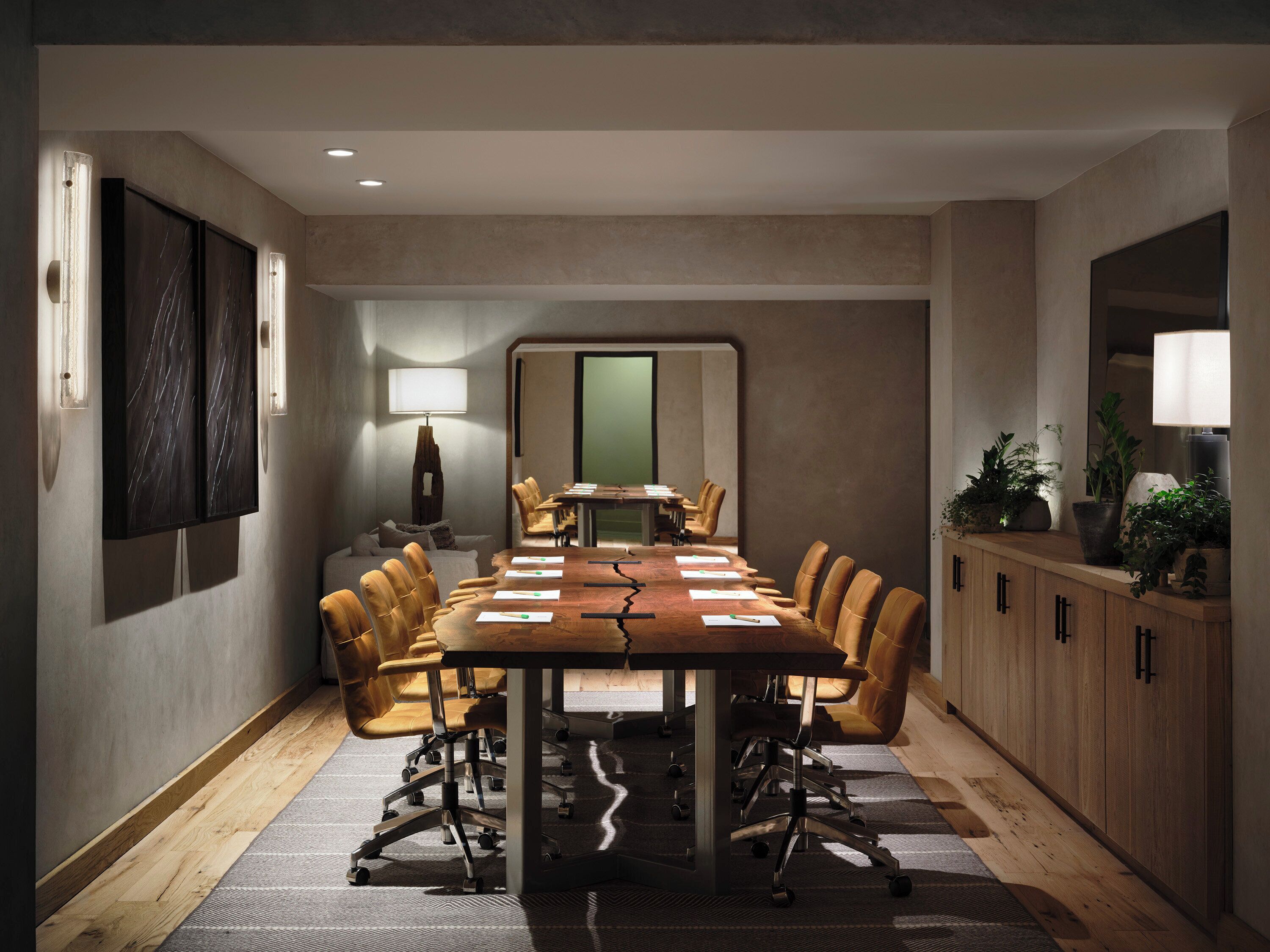 A conference room with a long table, chairs, a lamp, and a cabinet with plants.