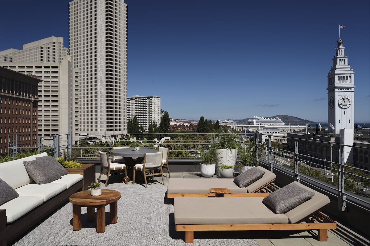 Eine Dachterrasse mit einer Couch, Liegestühlen, einem Tisch und Topfpflanzen.