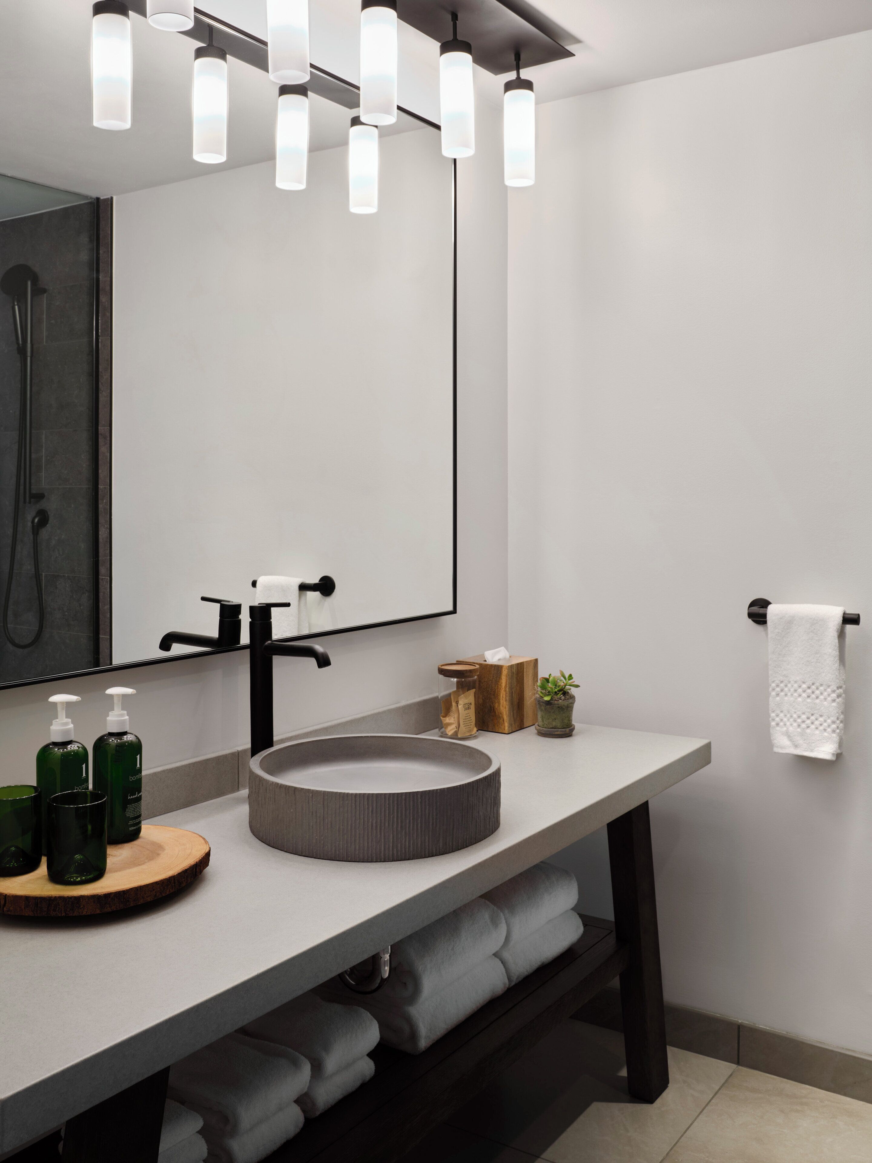 A modern bathroom with a round sink, black faucets, a large mirror, and a towel rack.