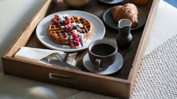 A breakfast tray on a bed with waffles, croissants, fruit, coffee, and juice.