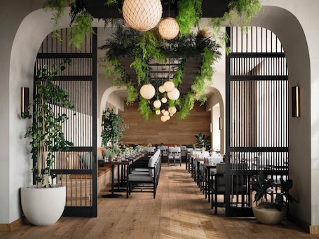 A restaurant with wooden flooring, black chairs, white tables, hanging plants, and pendant lights.. 1 Hotel San Francisco