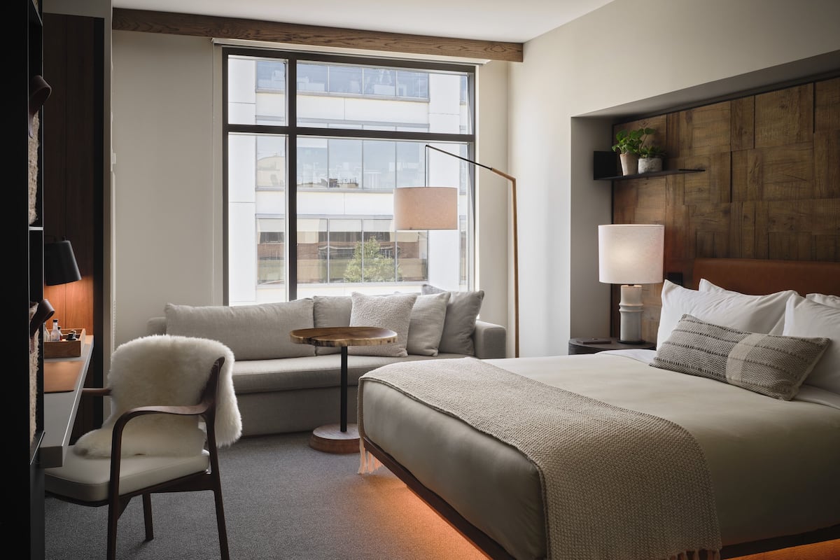 Ein modernes Hotelzimmer mit einem großen Bett, einer Couch, einem Sessel, einem kleinen runden Tisch und einer Stehlampe.