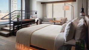Habitación de hotel con cama, escritorio, sofá, ventana con vista a una torre de reloj y una escalera.