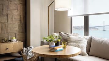 A modern living room with a round wooden table, a sofa, a floor lamp, and a view of a bridge.