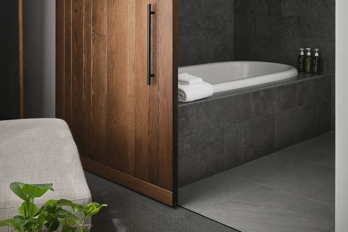 Ein modernes Badezimmer mit einem Holzschrank, einer Badewanne und einer Wandleuchte.
