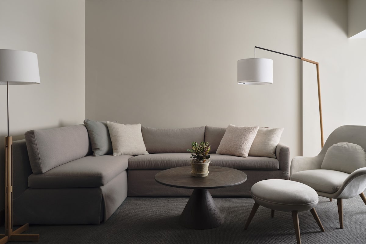 Ein modernes Wohnzimmer mit einem Ecksofa, einem runden Couchtisch, einem Beistelltisch und einer Stehlampe.