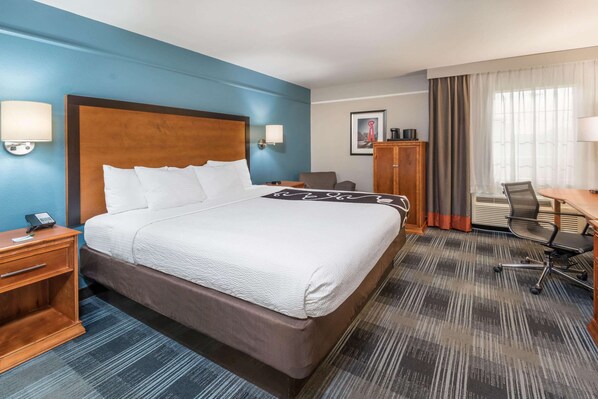 A hotel room with a large bed, a desk, a chair, a wardrobe, and a window with curtains.