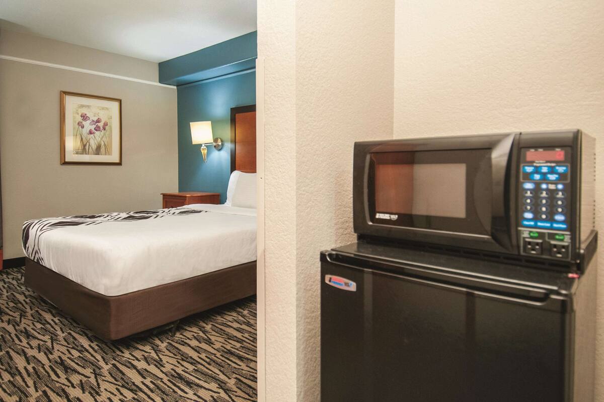 A hotel room with a bed, a wall-mounted lamp, and a microwave.
