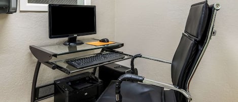 Una silla de oficina moderna con respaldo alto y apoyabrazos, un escritorio de cristal con monitor de computadora, teclado y ratón, además de una impresora.