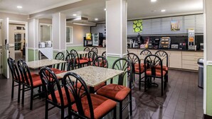 A restaurant with multiple tables and chairs, a kitchen area with appliances, and a counter with food items. - La Quinta Inn by Wyndham San Antonio Brooks City Base (San Antonio)