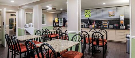 A restaurant with multiple tables and chairs, a kitchen area with appliances, and a counter with food items.