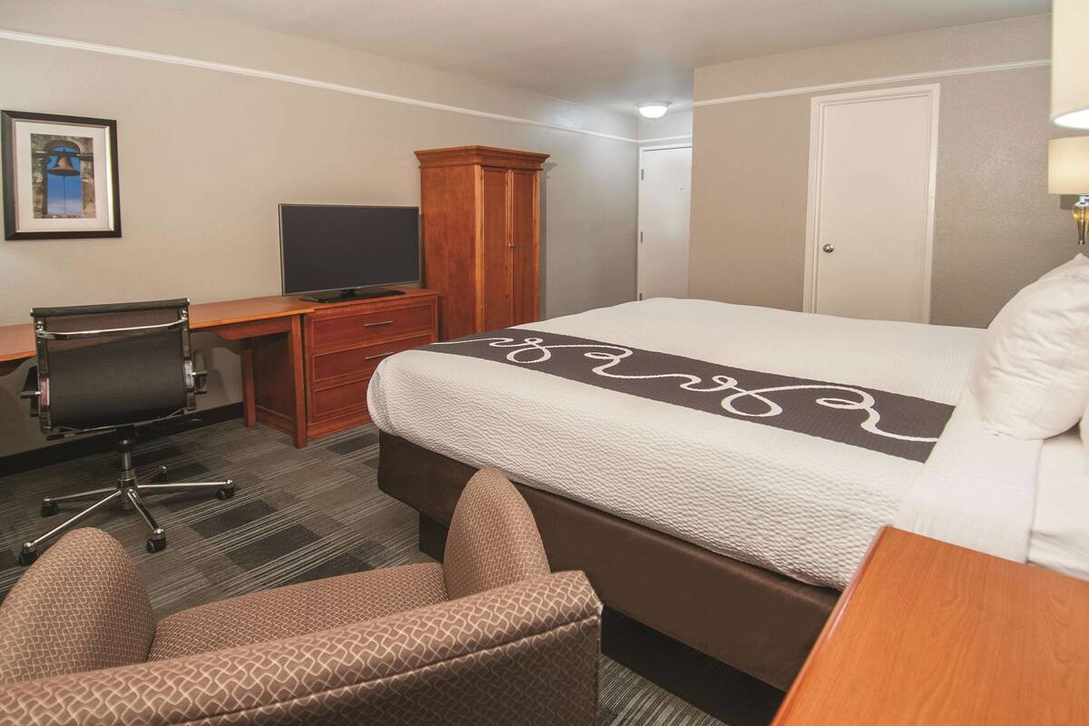 A hotel room with a bed, a desk, a chair, a television, and a wardrobe.