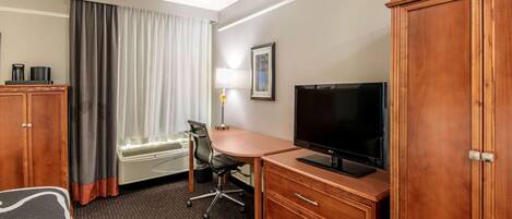 Habitación de hotel con cama, escritorio con televisor, silla, armario y ventana con cortinas.