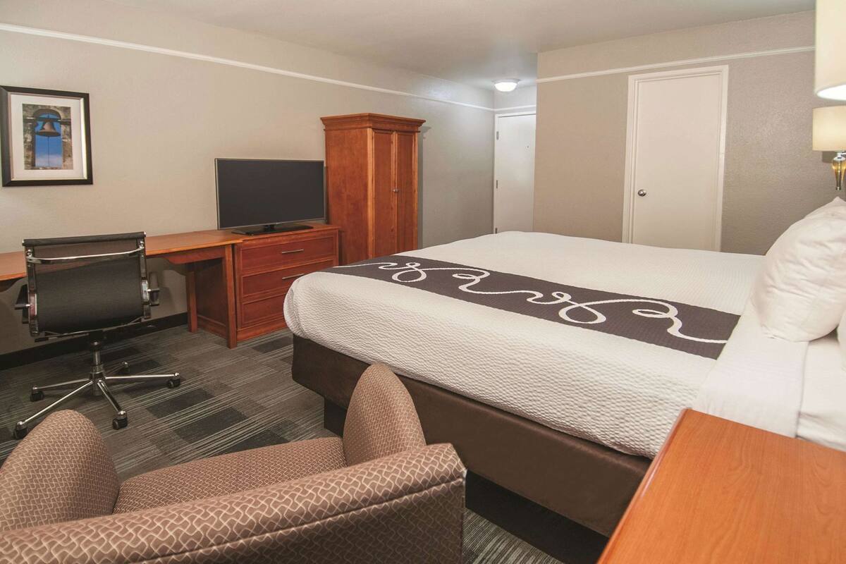 A hotel room with a bed, a desk with a chair, a television, a wardrobe, and a door.