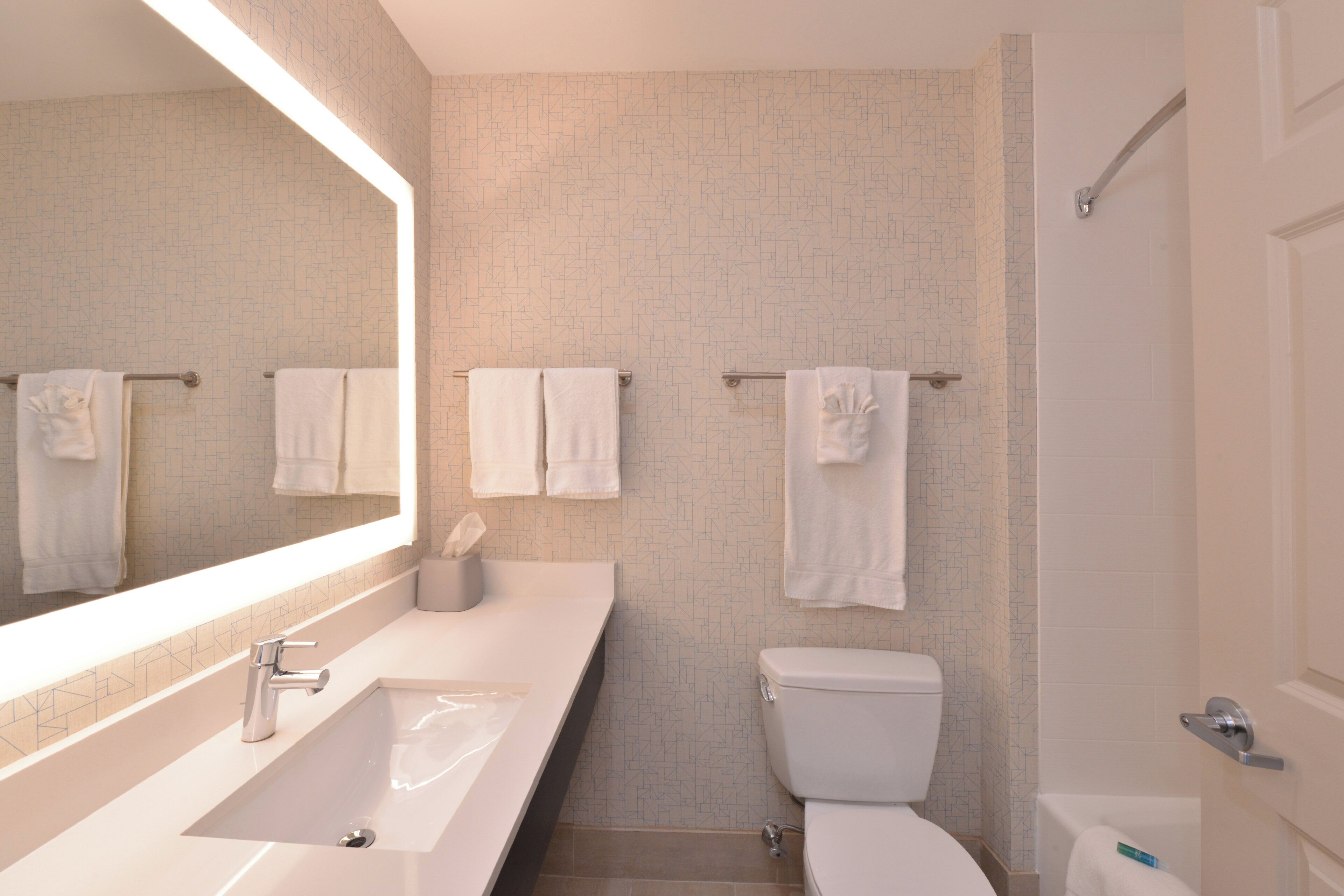 Ein modernes Badezimmer mit einem großen Spiegel, einem Waschbecken, einer Toilette und einem Handtuchhalter.